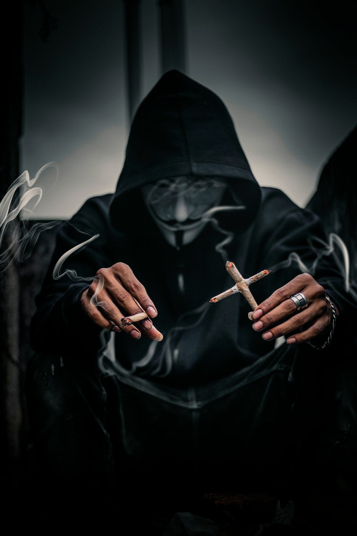 person in Guy Fawkes mask holding cross-shaped lighted cigarettes on his left with lighted joice on right hand