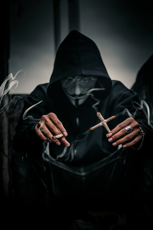 person in Guy Fawkes mask holding cross-shaped lighted cigarettes on his left with lighted joice on right hand